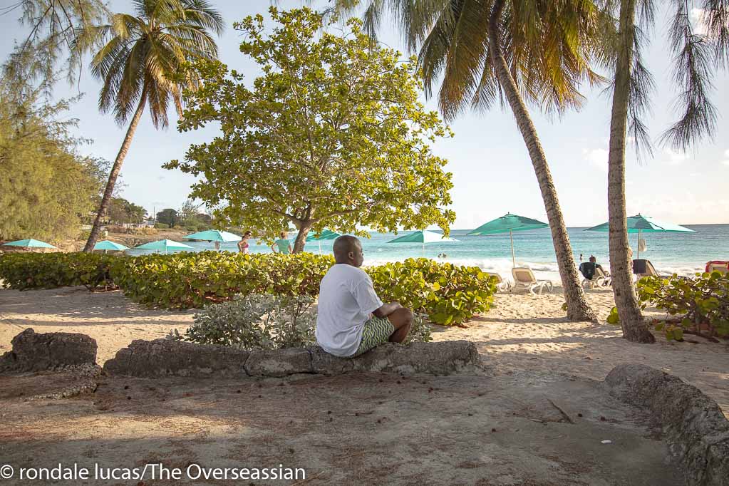 Rondale Lucas/The Overseassian sitting at Enterprise Beach Barbados. looking out to sea.